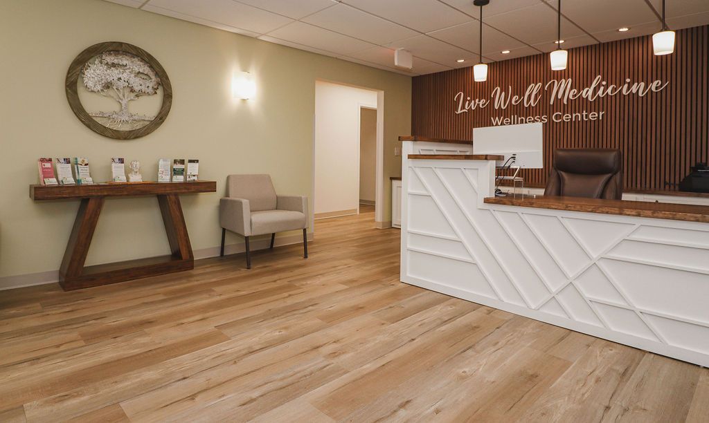 Broad view of Live Well Medicine Wellness Center reception area with front desk, welcoming seating, tree wall art, and hardwood floors